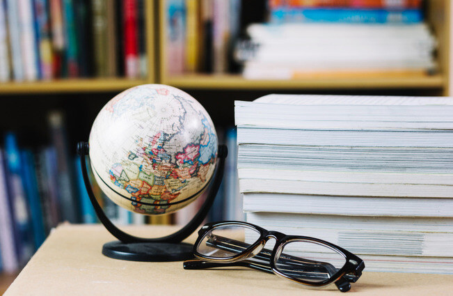 A globe next to some books and a pair of glasses