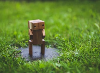 A wooden robot figures standing in a patch of grass